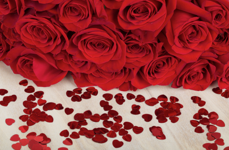 a bouquet of red roses and red hearts sprinkled on a table